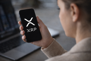 Person holding a smartphone displaying the XRP cryptocurrency logo while checking digital asset markets.